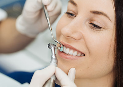 A woman is receiving a dental cleaning. A dentist uses dental tools while the patient smiles.