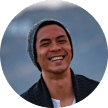 A person wearing a beanie and sweater is smiling in an outdoor setting.