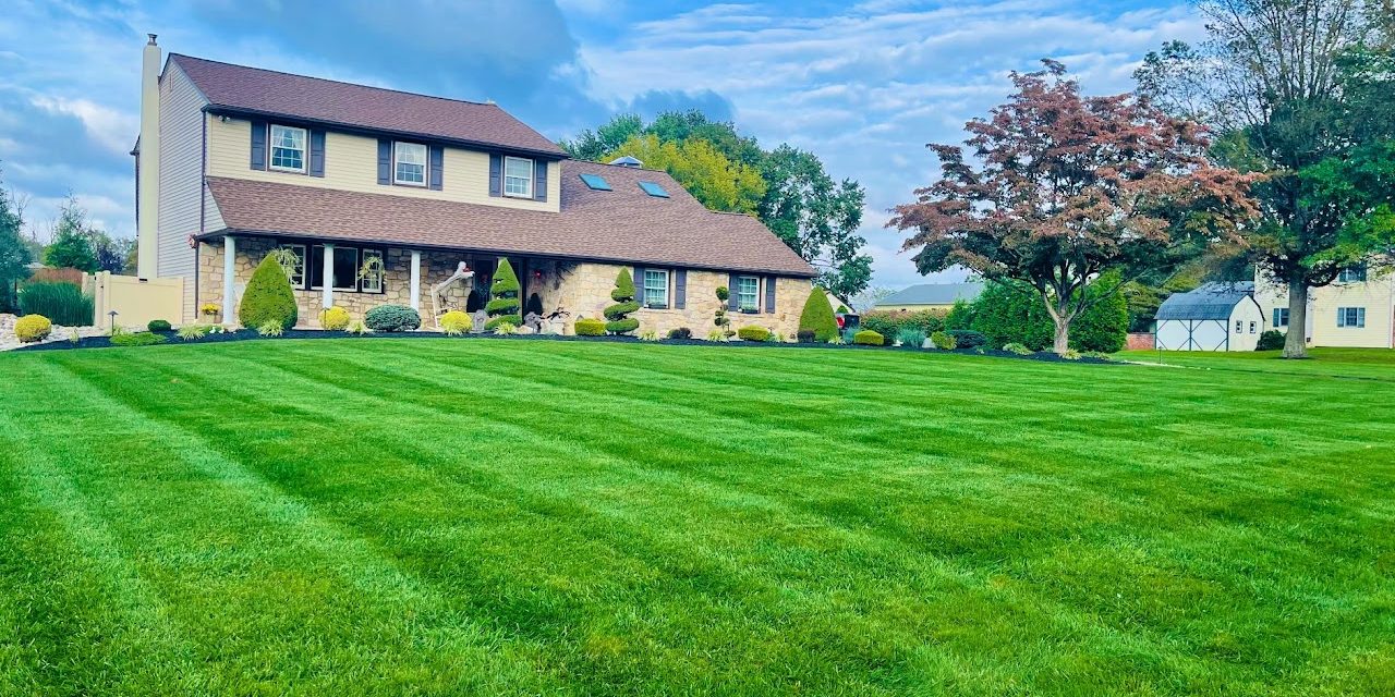 A two-story house with a well-maintained lawn and landscaping, situated under a blue sky with scattered clouds.